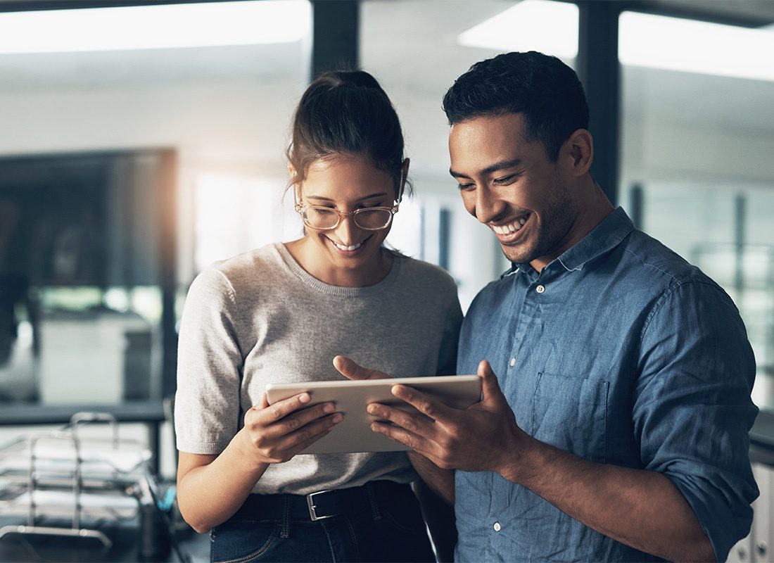 Service Center - Portrait of a Cheerful Young Male and Female Coworkers Looking at a Tablet While Standing in the Office